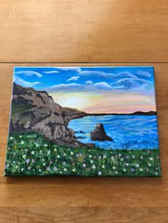 an acrylic painting of the ocean with flowers and rocks in the foreground