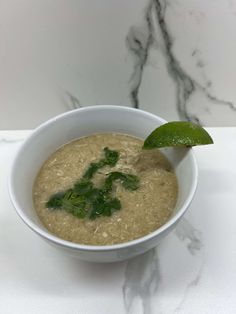 a white bowl filled with soup sitting on top of a marble counter next to a green leaf