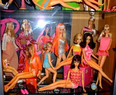 several barbie dolls are on display in a glass case with pink and orange outfits,