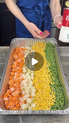 a woman standing in front of a metal tray filled with vegetables and veggies