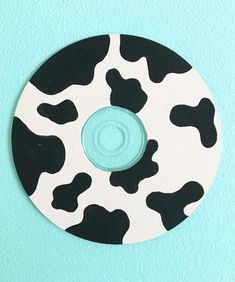 a black and white cow print disk on a blue background with a button in the center