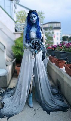 a woman dressed as corpse bride with blue hair and make - up holding flowers in her hands