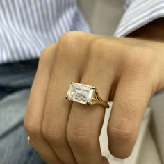 a person wearing a ring with an emerald cut diamond on it's middle finger