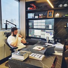 a man sitting at a desk in front of a computer monitor and keyboard, talking on the phone