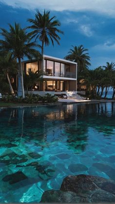 a large house sitting on top of a lush green hillside next to the ocean at night