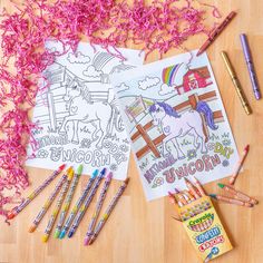 coloring books and crayons on a wooden table with pink shredded paper next to them