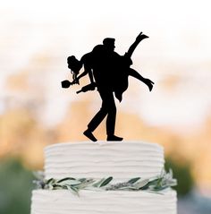 the silhouette of a man carrying a woman is on top of a wedding cake with greenery