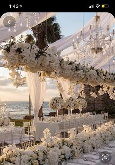 an outdoor wedding setup with white flowers and chandeliers at the head table, overlooking the ocean