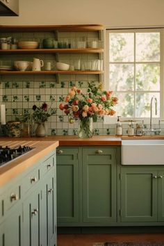 a kitchen filled with lots of green cupboards and flowers on top of the counter