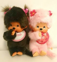 two little dolls are posed next to each other on a white surface, one is wearing a pink and black outfit