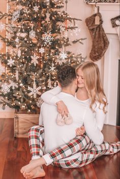 a man and woman sitting in front of a christmas tree with their arms around each other