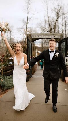 a bride and groom are walking down the sidewalk holding their hands in the air as they hold flowers