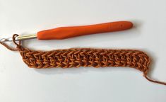 an orange crochet hook is laying on the table next to a piece of yarn