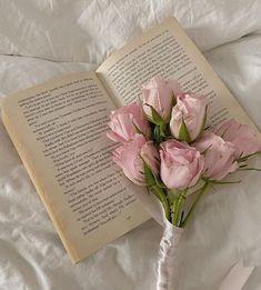 a bouquet of pink flowers sitting next to an open book on top of a bed