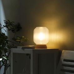 a white lamp sitting on top of a table next to a plant