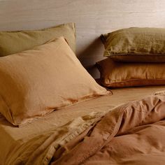 pillows and blankets are stacked on top of each other in a bed with brown linens