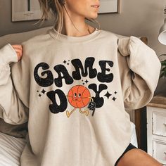 This makes the perfect vintage school spirit Game Day Basketball sweatshirt! Game Day Basketball! This basketball sweatshirt is great for the basketball moms and basketball lovers! This distressed basketball design is perfect on the popular Gildan brand sweatshirt. This vintage style sweatshirt will keep you warm throughout the football season! A pre-shrunk, classic fit sweater that's made with air-jet spun yarn for a soft feel and reduced pilling. ** P R O D U C T ** - 50% cotton, 50% polyester Basketball Gameday Outfit, Trendy School Spirit Shirts, Mom Basketball Game Outfit, Basketball Game Day Shirts, Retro Graphic Print Sweatshirt For Game Day, Retro Sweatshirt For Game Day, Sports Season, Retro Sweatshirt For Game Day And Sports Season, Retro Game Day Sweatshirt With Letter Print, Basketball Cotton Sweatshirt For Sports Season