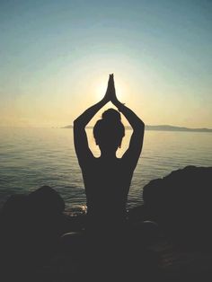 a person sitting in front of the ocean with their hands up while doing yoga exercises