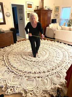 an older woman measuring the length of a crocheted bedspread in her living room