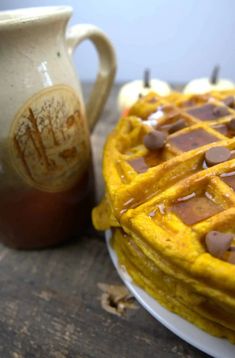 a stack of waffles on a plate next to a mug