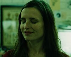 a woman with long brown hair and red shirt looking at something on the wall behind her