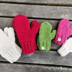 three knit mittens sitting on top of a wooden bench