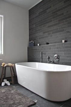 a large white bath tub sitting in a bathroom next to a wooden stool and window