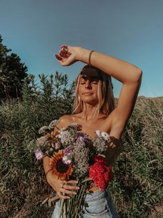 a woman is holding flowers in her hand and posing for the camera with one arm behind her head