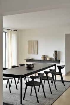 a dining room table with chairs and a bowl on it in front of a window