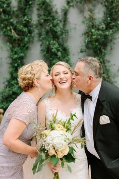 the bride and groom are kissing each other outside with greenery on the wall behind them