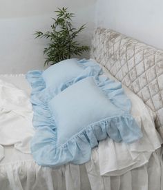 a bed with blue ruffled pillows on top of it and a plant in the corner