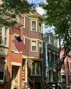 an american flag is flying in front of some houses on a street with parked cars