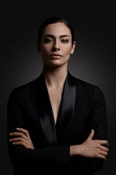 a woman with her arms crossed posing for a photo in front of a black background