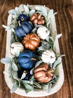 some pumpkins and leaves are in a white bowl