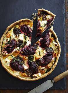 a pizza with beets and cheese on it next to a knife