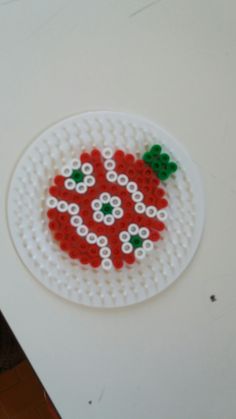 a white plate with red and green beads on it sitting on top of a table