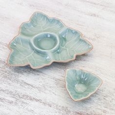 two green leaf shaped dishes sitting on top of a wooden table next to each other