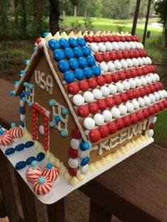 a gingerbread house decorated with red, white and blue decorations on a wooden fence