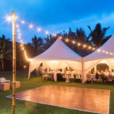 a dance floor is set up in the middle of a lawn with white tents and string lights