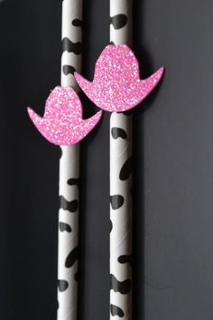 two paper straws decorated with pink and black glitter hats on top of each other