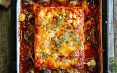 a casserole dish with meat, cheese and mushrooms in it on a wooden table