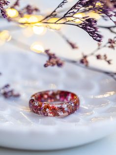 a wedding ring sitting on top of a white plate next to purple flowers and lights