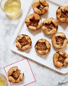 mini meat pies on a white tray next to a glass of beer