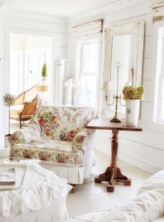 a living room filled with white furniture and flowers on the couches in front of two windows