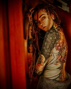 a woman with dreadlocks and tattoos on her body is leaning against a wall