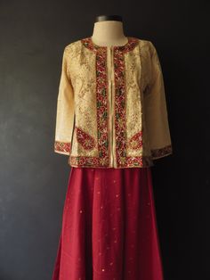 "I'm not sure, but I think the outfit is made of dupion silk. The top/jacket/kameez is heavily embroidered on the front and cuffs with metallic thread (Zardozi embroidery), beads and sequins. It's flared at the bottom, has side slits and hook-and-eye closure up the front. The voluminous skirt/salwar has a sheen to it and has gold thread dot pattern woven into it, with a metallic gold trim on the hem. It has a drawstring waist with a side zipper. The saree/dupatta is made from the same fabric. Bo Transitional Silk Choli With Resham Embroidery, Fitted Straight Kurta Choli With Intricate Embroidery, Festive Bollywood Tussar Silk Choli, Fitted Chinon Traditional Wear With Long Sleeves, Embroidered Anarkali Tussar Silk Choli, Transitional Raw Silk Choli With Cutdana, Raw Silk Lehenga With Straight Kurta For Transitional Season, Festive Anarkali Choli In Tussar Silk, Transitional Unstitched Raw Silk Choli