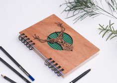 a wooden notebook with an image of a deer on it and three pencils next to it