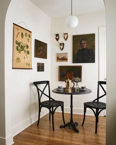 two chairs and a table in a room with pictures on the wall behind them,