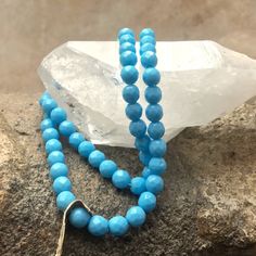 a blue beaded necklace sitting on top of a rock next to a crystal point