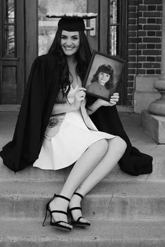 a woman sitting on the steps with her graduation cap and gown over her head, holding a framed photo